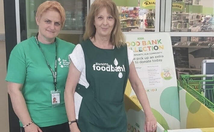 Barking Foodbank employee and volunteer standing inside Asda during a food drive, collecting donations to support local people in need.