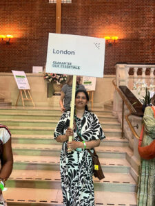 Gowry Paraneeharan, Senior Welfare Rights Adviser at Hope Family Trust/Barking Foodbank holding gurantee our essentials placard